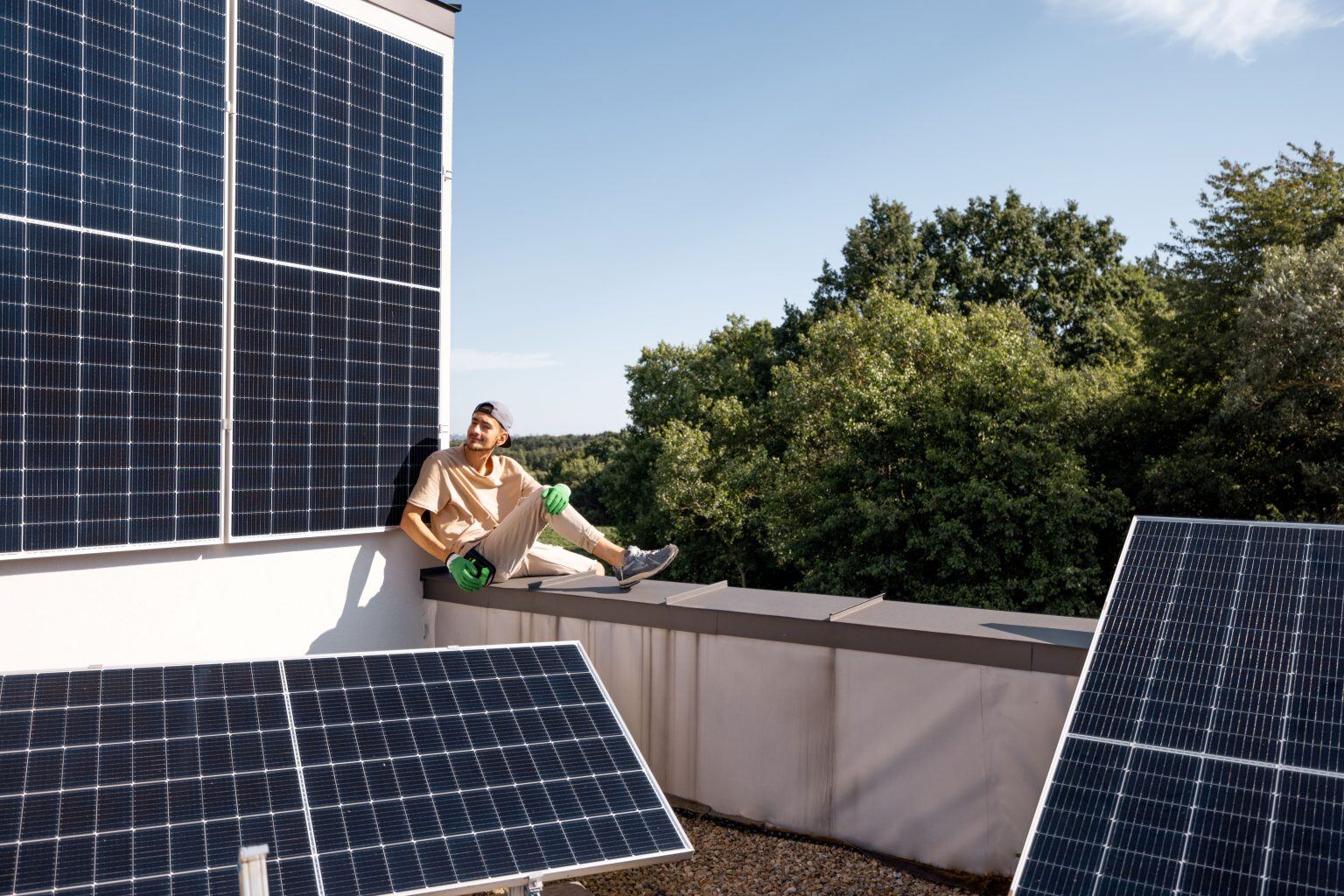 Man sitting on a rooftop with large solar panels under a clear sky.